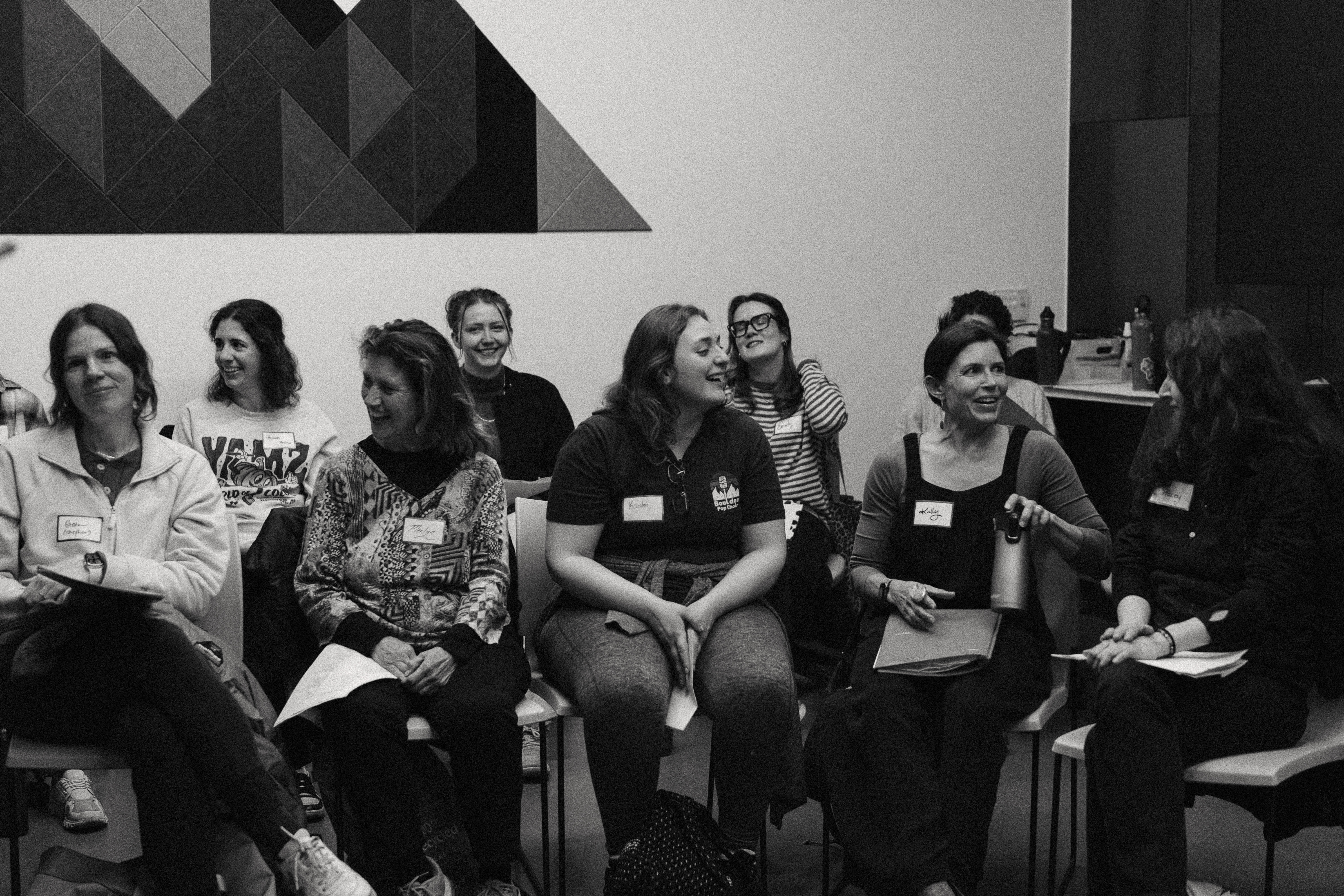 Choir members laughing together while seated in rows at a rehearsal, in black and white.